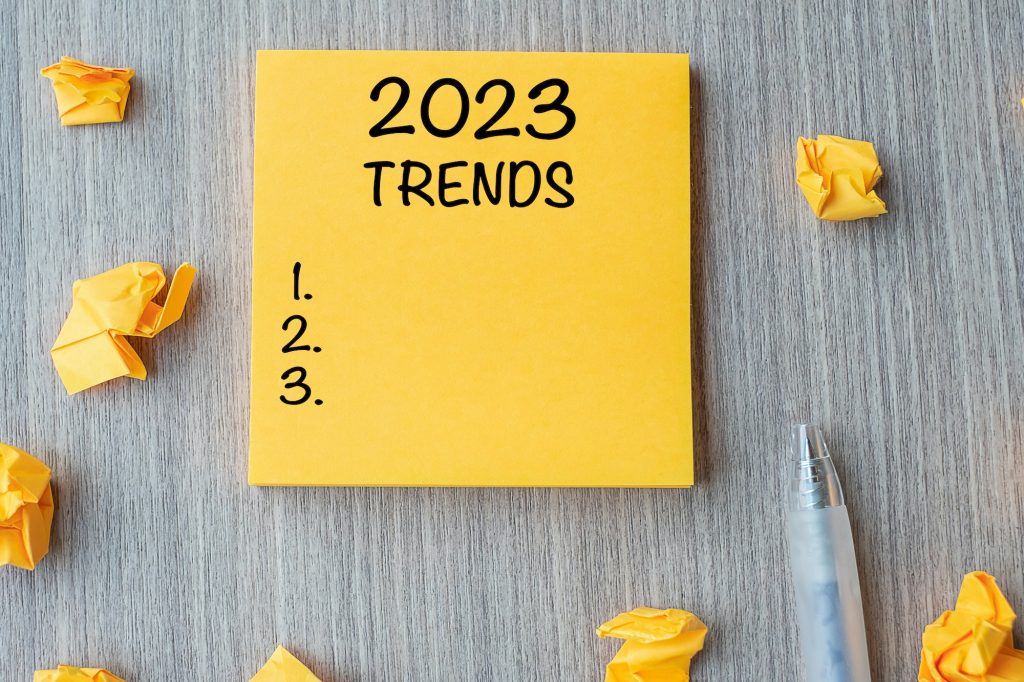 2023 Trends word on yellow note with pen and crumbled paper on wooden table background.