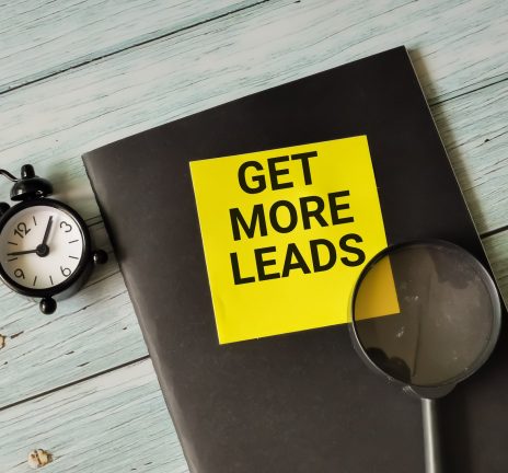 Phrase get more leads written on sticky note with alarm clock,magnifying glass and book.